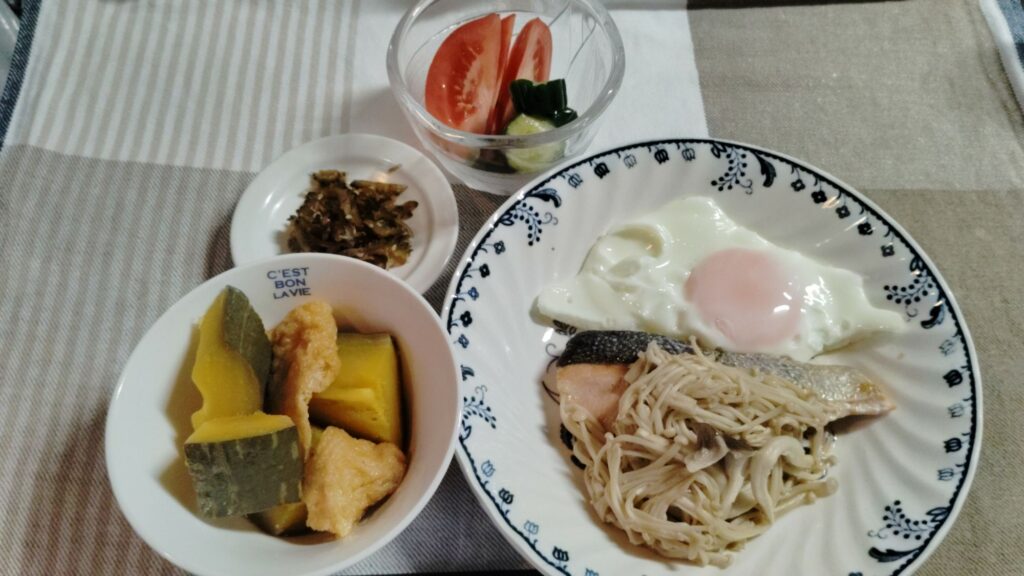 鮭のバター焼き・えのきソテー、目玉焼き、かぼちゃとあげの煮物、ゴーヤの佃煮、きゅうり漬け、トマト。