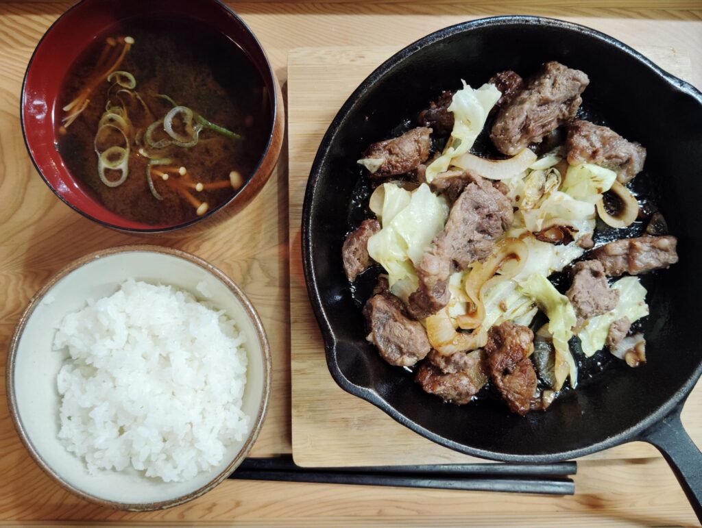 ごはん。タレ漬け肉のスキレット焼き(玉ねぎ、キャベツ)。赤だしみそ汁(わかめ、えのき)。