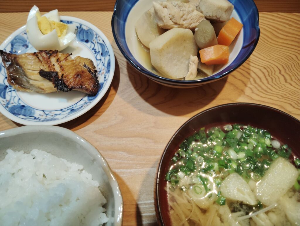 ごはん。ほっけの切り身干し。ゆで卵。鶏肉と里芋の煮物(ごぼう、人参、大根)。みそ汁(エノキ、あげ、わかめ、ねぎ)。