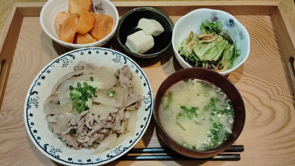 牛丼(ねぎ、しょうが)。みそ汁(あげ、ねぎ、わかめ、えのき)。チシャの酢味噌和え(レタス、ちくわ)。高野豆腐。柿。
