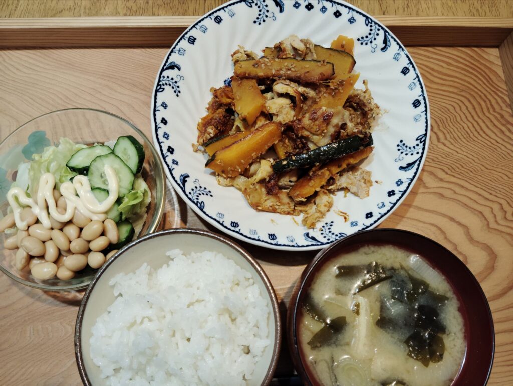ご飯。かぼちゃと豚肉の甘辛炒め。大豆サラダ（レタス、キュウリ）。みそ汁（あげ、わかめ、長ネギ）。