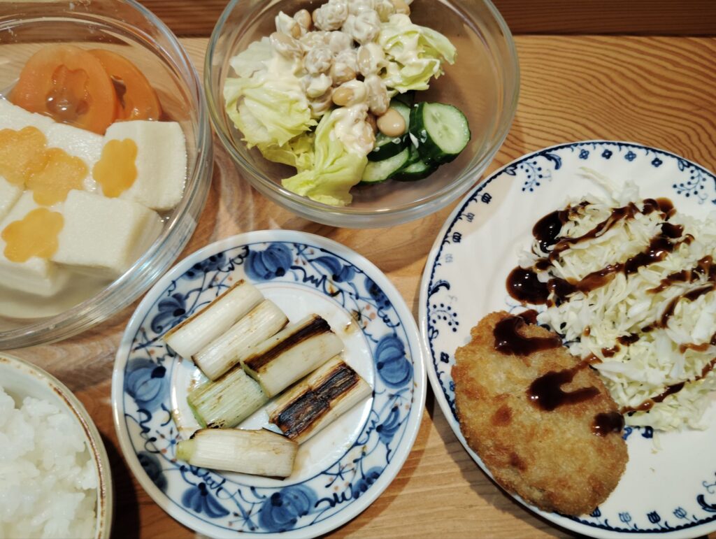 ご飯。コロッケ、キャベツ。長ネギ焼き。高野豆腐、人参。大豆サラダ、レタス、キュウリ。