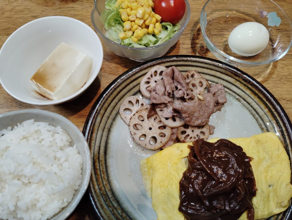 ご飯。オムレツ、ハヤシライスソース。牛肉とれんこん炒め。サラダ（レタス、コーン、トマト）冷奴。ゆでたまご。