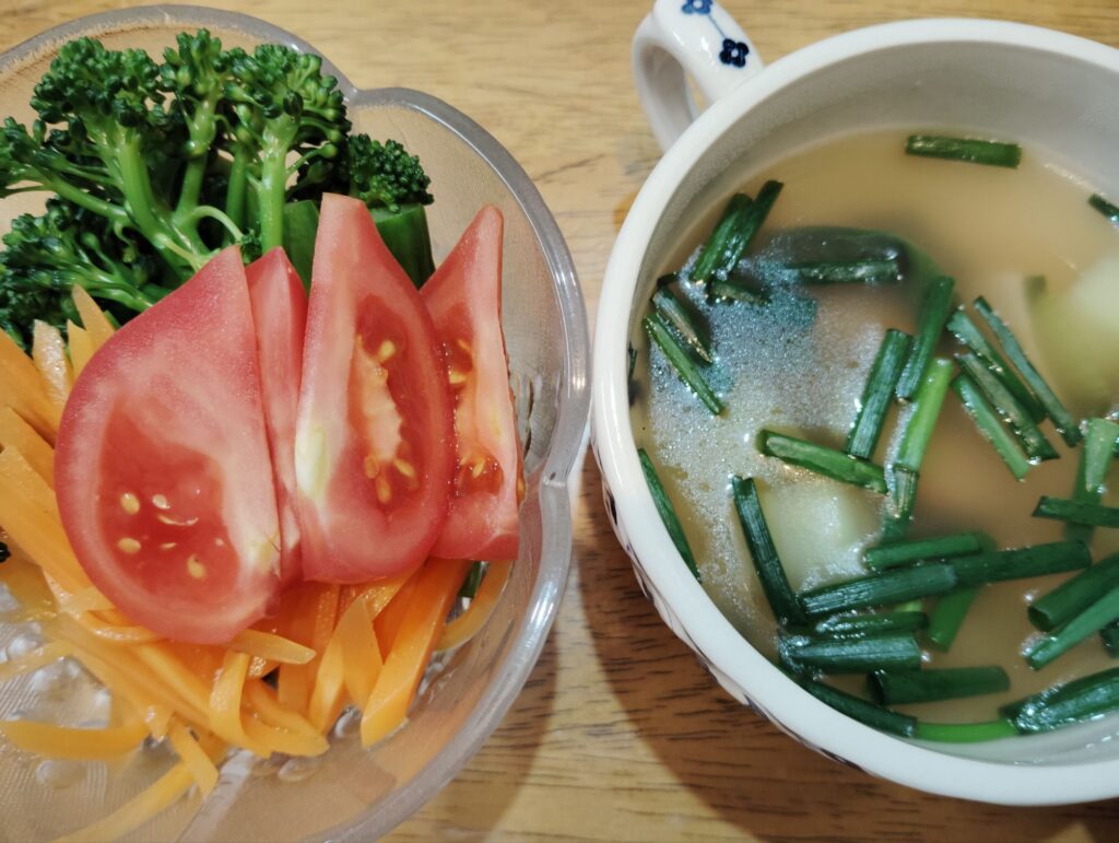 青梗菜のスープ（ハム、ねぎ）。サラダ（人参ラぺ、ゆでブロッコリー、トマト）。