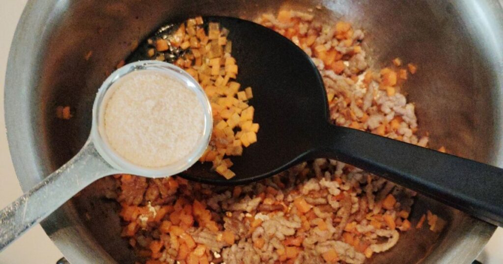 合びき肉に人参を加えて炒め、砂糖を入れる様子