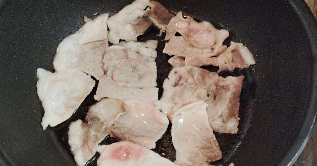 熱したフライパンに油を敷き豚肉を炒める様子